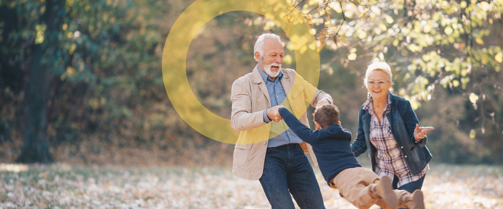 Two smiling grandparents and a young grandchild playing and enjoying an autumn day